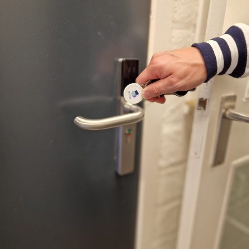 Hand met keyfob opent deur voorzien van digitaal deurbeslag voor veilige en eenvoudige toegang